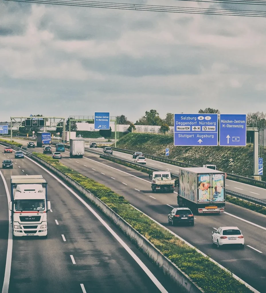 Autobahn mit mehrspurigem Verkehr, blaue Wegweiser zu Salzburg, München und anderen Städten, Lastwagen und PKW.